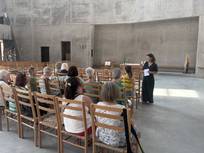 Barbara Schatz erklärt den auf Stühlen sitzenden Teilnehmer*innen der Kirchenführung die architektonischen Besonderheiten in der Kirche.